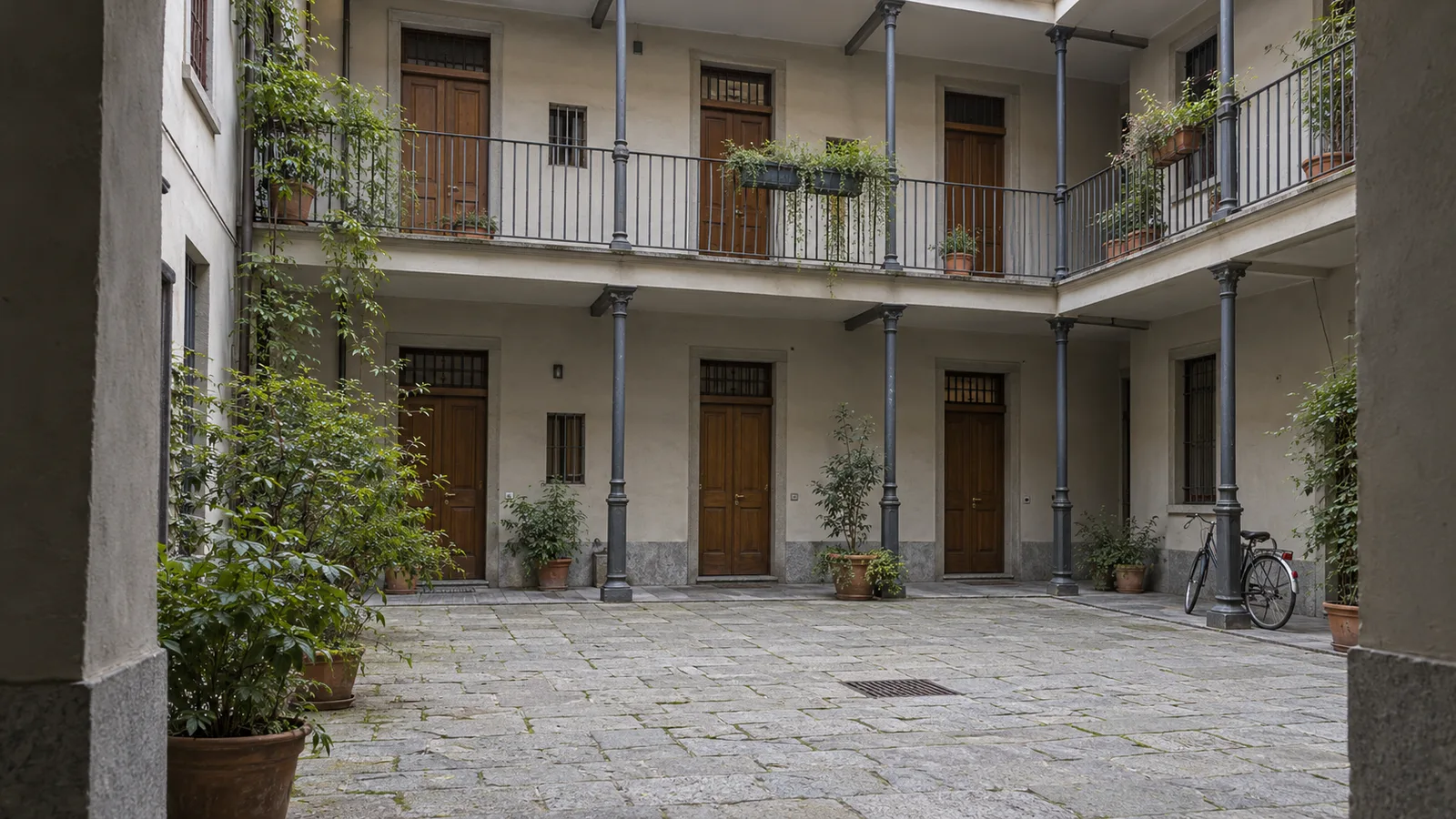 Cortile di una casa di ringhiera milanese restaurata, con due piani di ballatoi e parapetti in ferro