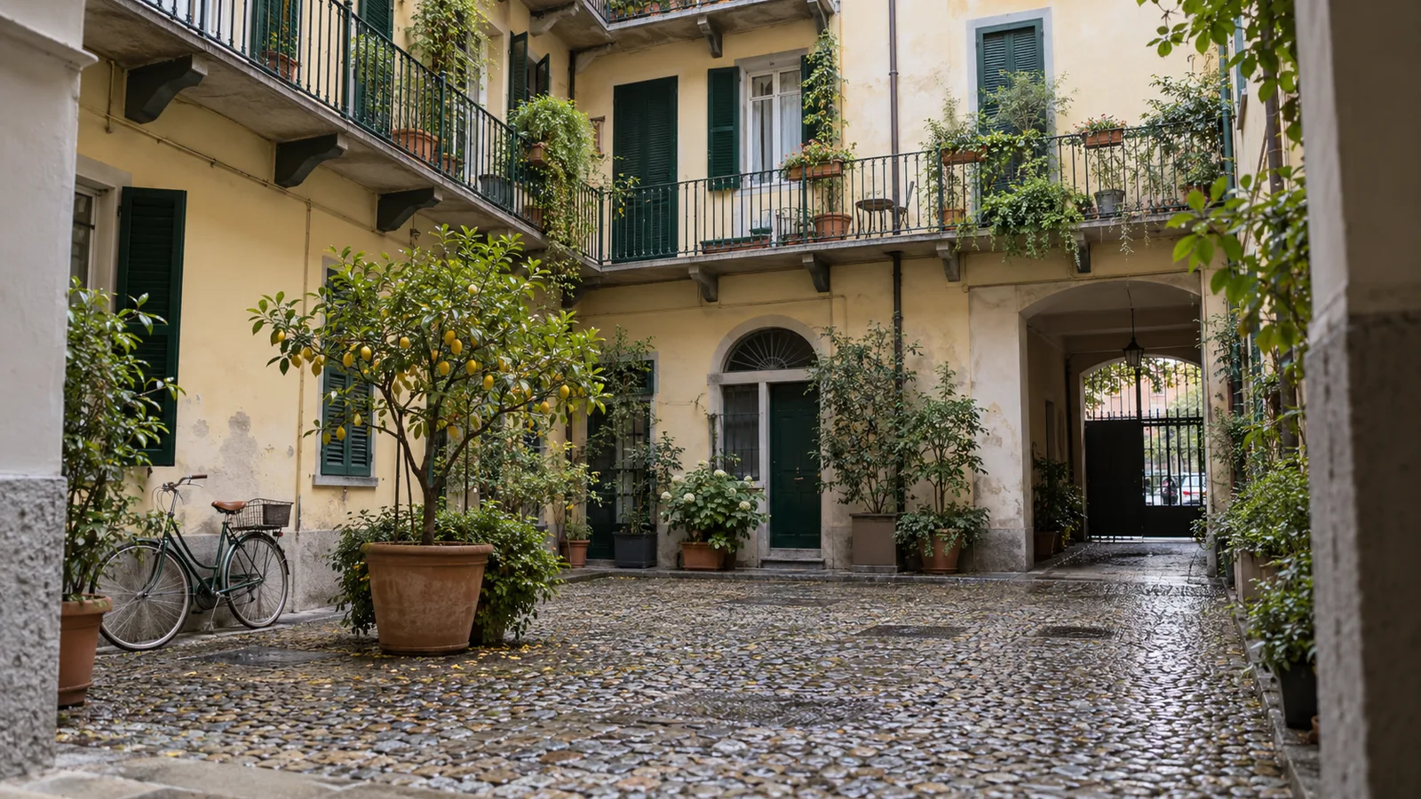 Cortile di una casa di ringhiera milanese restaurata, con ringhiere verdi e un limone in vaso